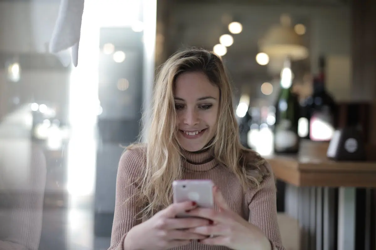 Woman smiling while checking her phone at a warmly lit cafe
