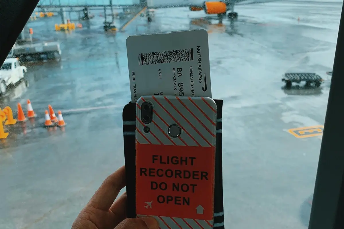 Traveler holding phone and boarding pass at airport gate with planes visible through the window