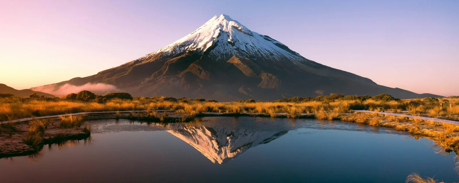 Snow-capped Mount Taranaki reflected in Pouakai Tarns in golden light, New Zealand