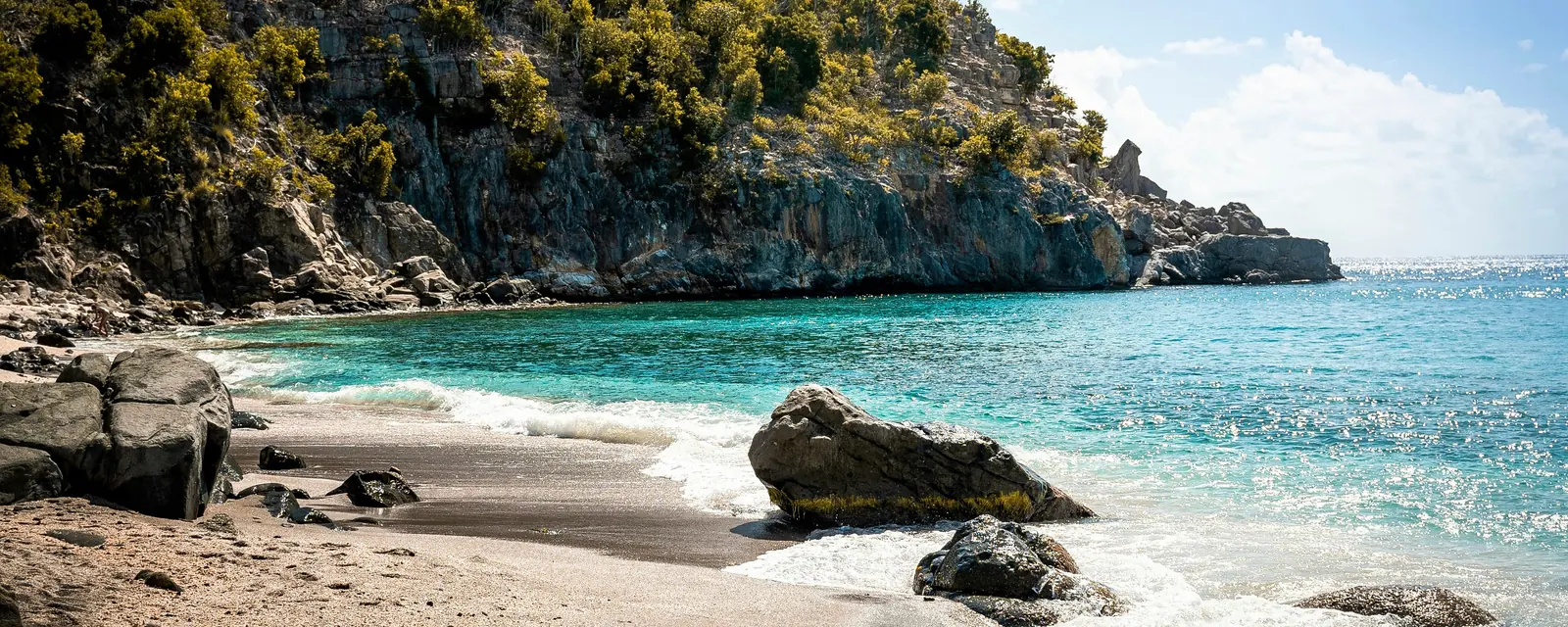 Clear turquoise water beside the rocky green headland at Shell Beach in Gustavia, Saint Barthรฉlemy