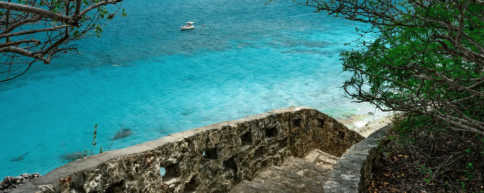 Stone steps framed by trees descending toward turquoise Caribbean water at 1000 Steps on Bonaire