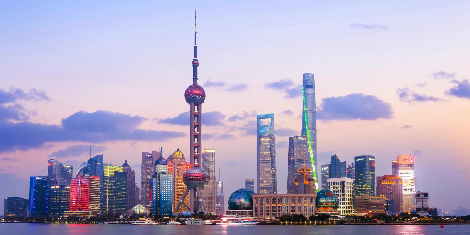 Shanghaiβs Oriental Pearl Tower and Pudong skyline glowing beneath a pink and lavender sky across the Huangpu River