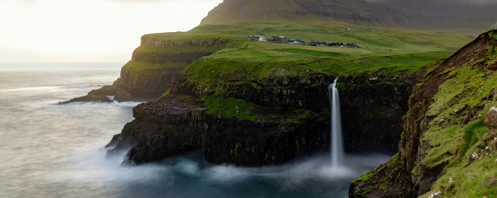 Sunrise light over Múlafossur Waterfall and the sea cliffs at Gásadalur in the Faroe Islands