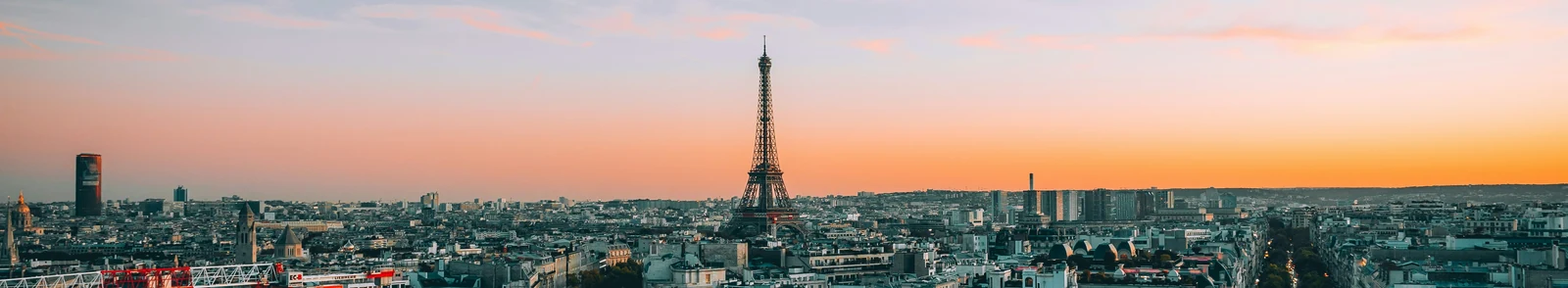 The Eiffel Tower above Paris rooftops beneath a peach-colored sunset