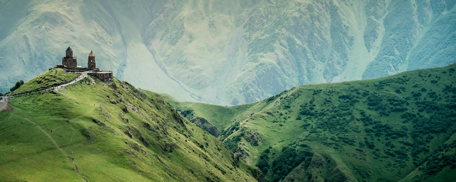 Gergeti Trinity Church on a sunlit green ridge in the Caucasus Mountains of Georgia