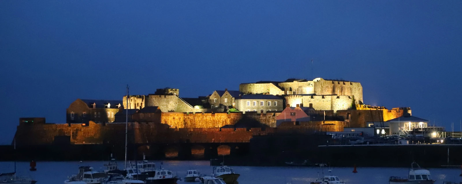 Illuminated Castle Cornet above boats in Saint Peter Port harbour at blue hour