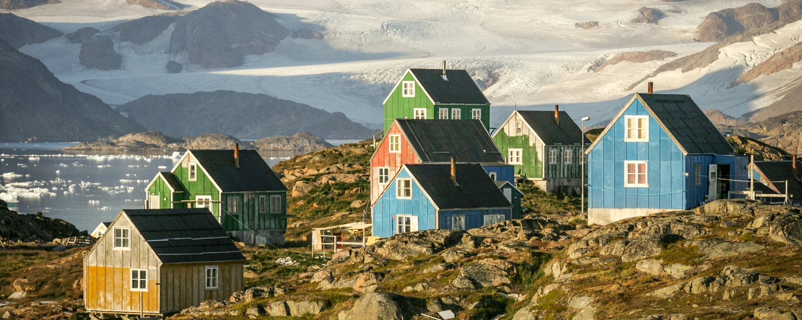 Colorful houses on the fjord near Kulusuk beneath glacier-covered mountains in East Greenland