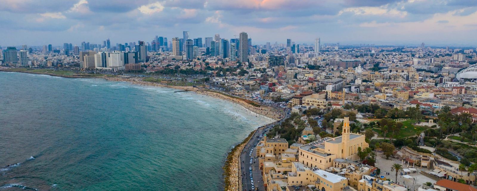 Historic waterfront buildings beside the curving beach and skyline of Tel Aviv