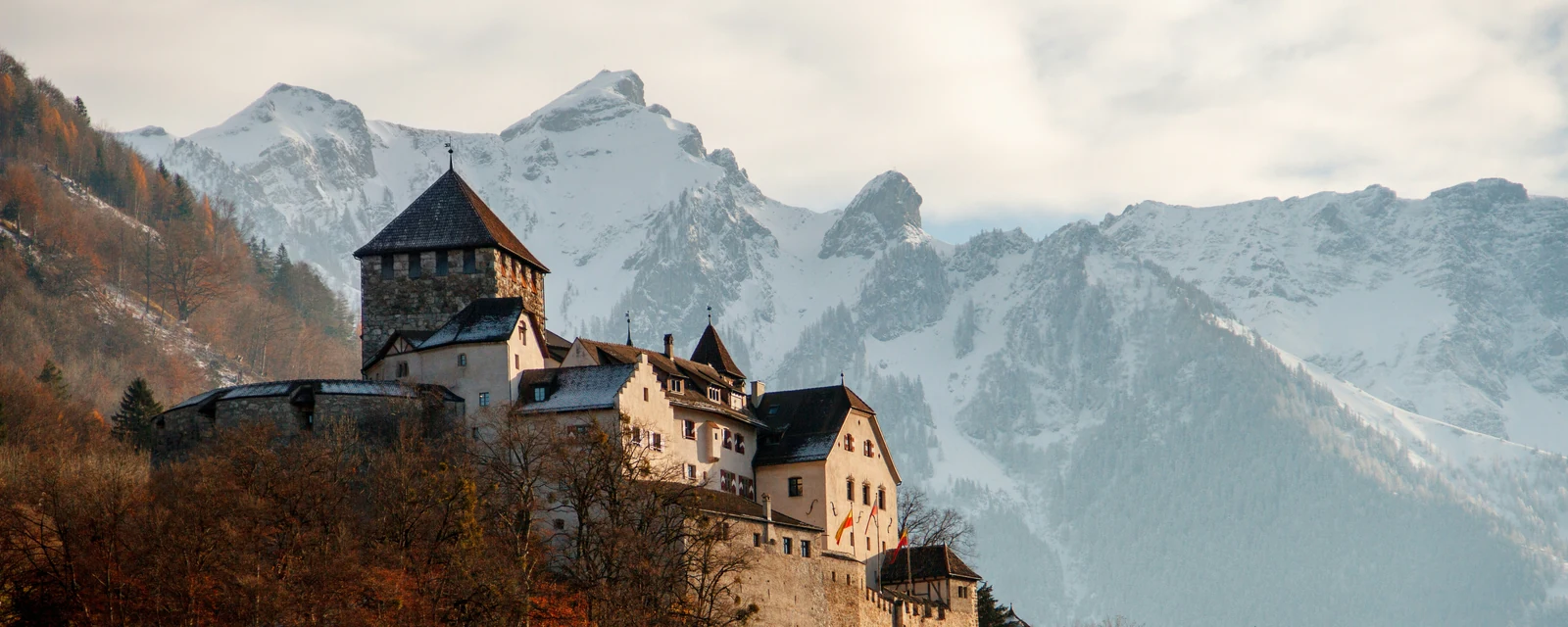 Vaduz Castle above autumn trees with snow-covered Alps behind it in Liechtenstein