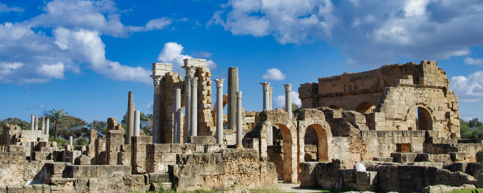 Ancient stone arches and Roman columns beneath a vivid blue sky at Leptis Magna, Libya