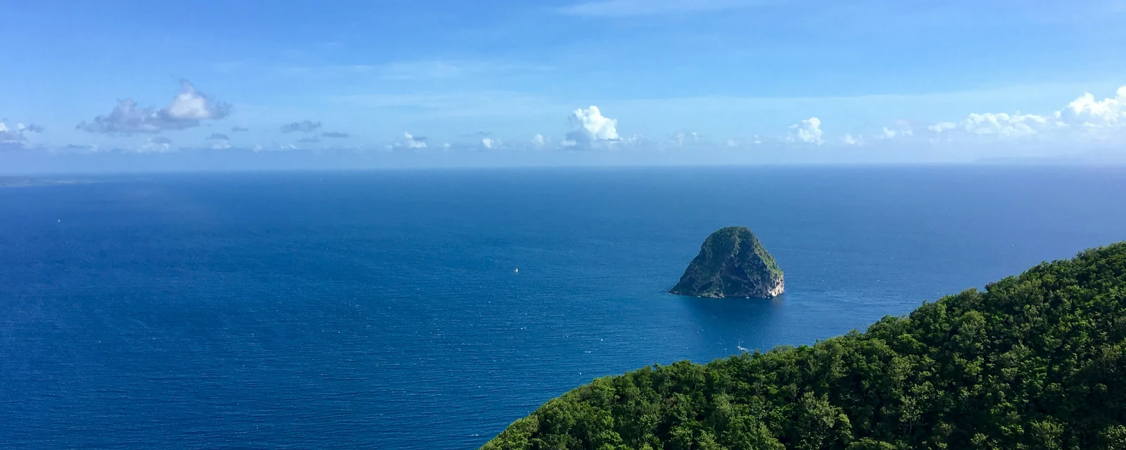 Diamond Rock rising from the deep blue Caribbean beyond a green coastal ridge in Martinique