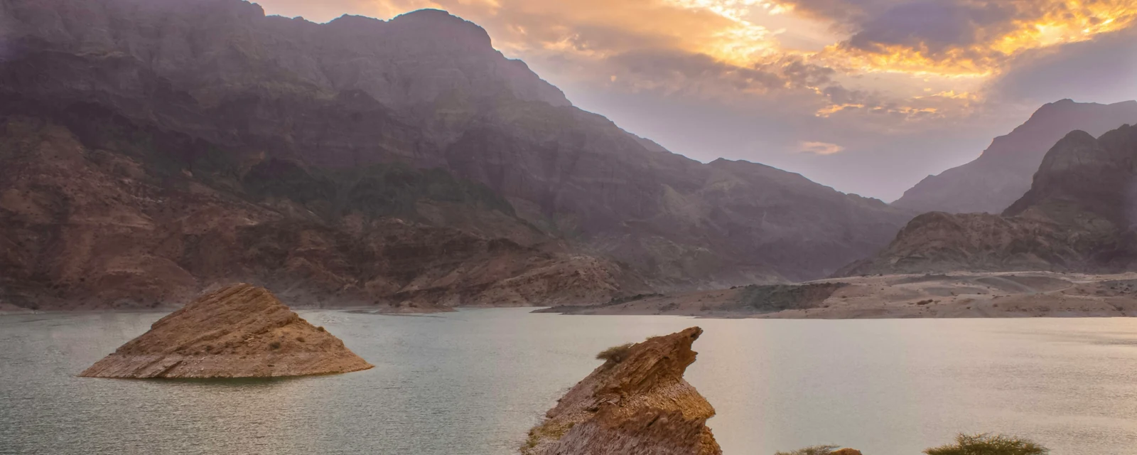 Sunset over mountain reservoir waters and rocky islands in Oman