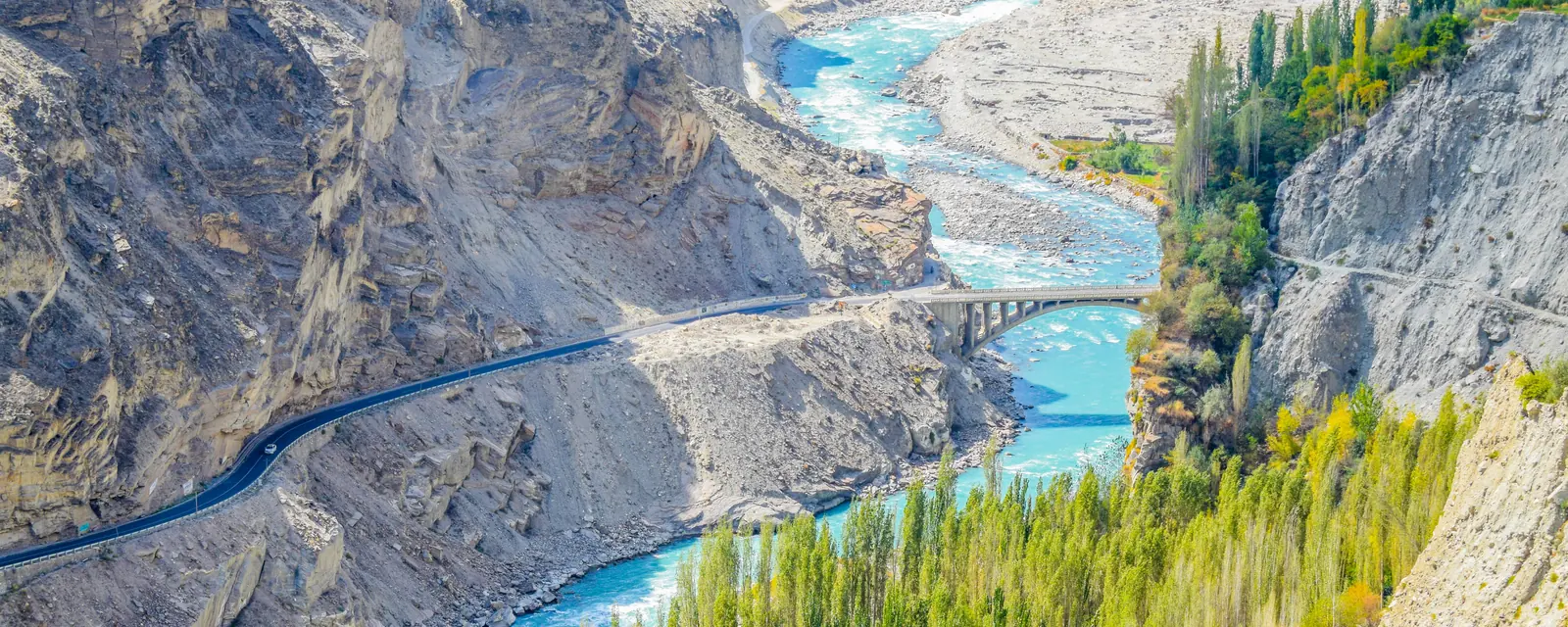 Turquoise river winding through Hunza Valley beside golden trees and the mountain road