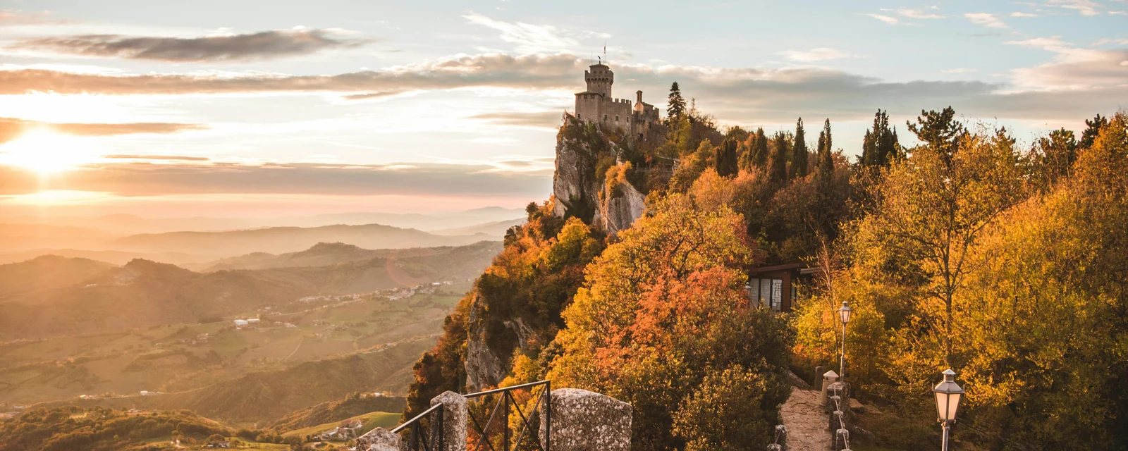 Autumn trees and a stone tower above the sunset-lit landscape of San Marino