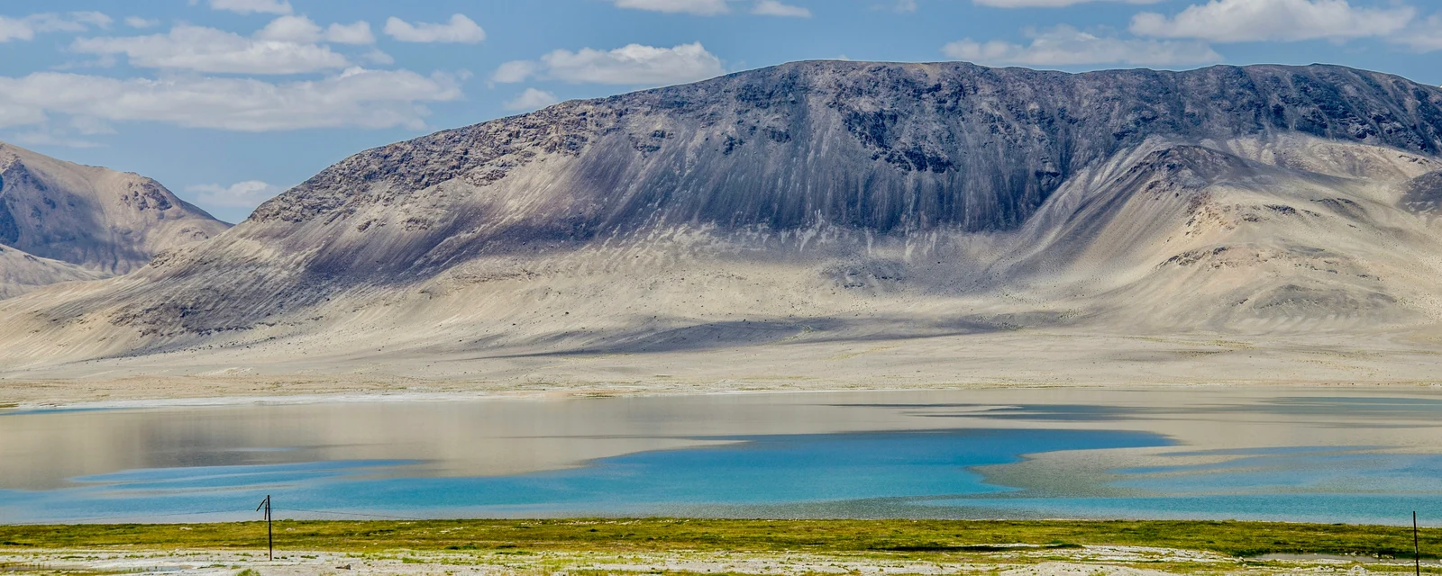 Blue alpine lake beneath the broad rocky ridges of the Pamir Mountains, Tajikistan