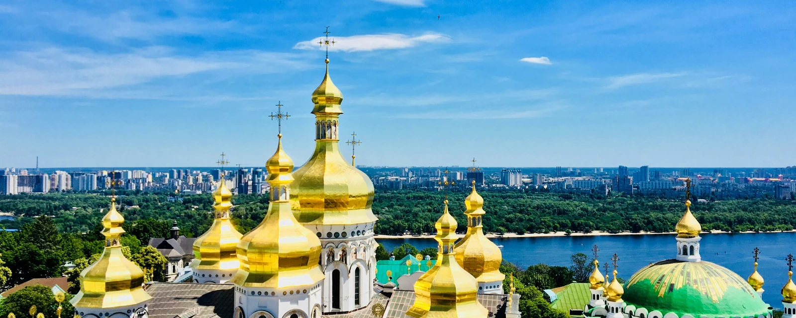 Golden church domes above the Dnipro River beneath a blue sky in Kyiv, Ukraine